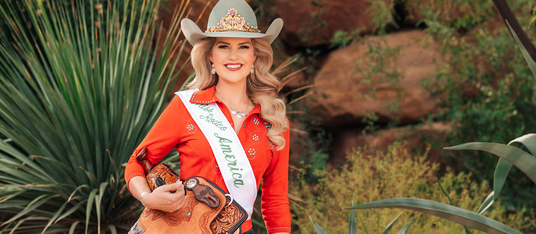 Miss Rodeo America 2024, Emma Cameron, wearing a cowboy hat, crown, and jeans, boots, and a western shirt.